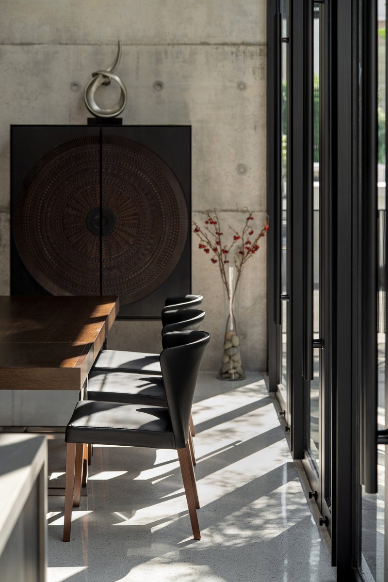 Dining chair and carved cabinet against exposed concrete wall with sunlight filtering through vertical screens