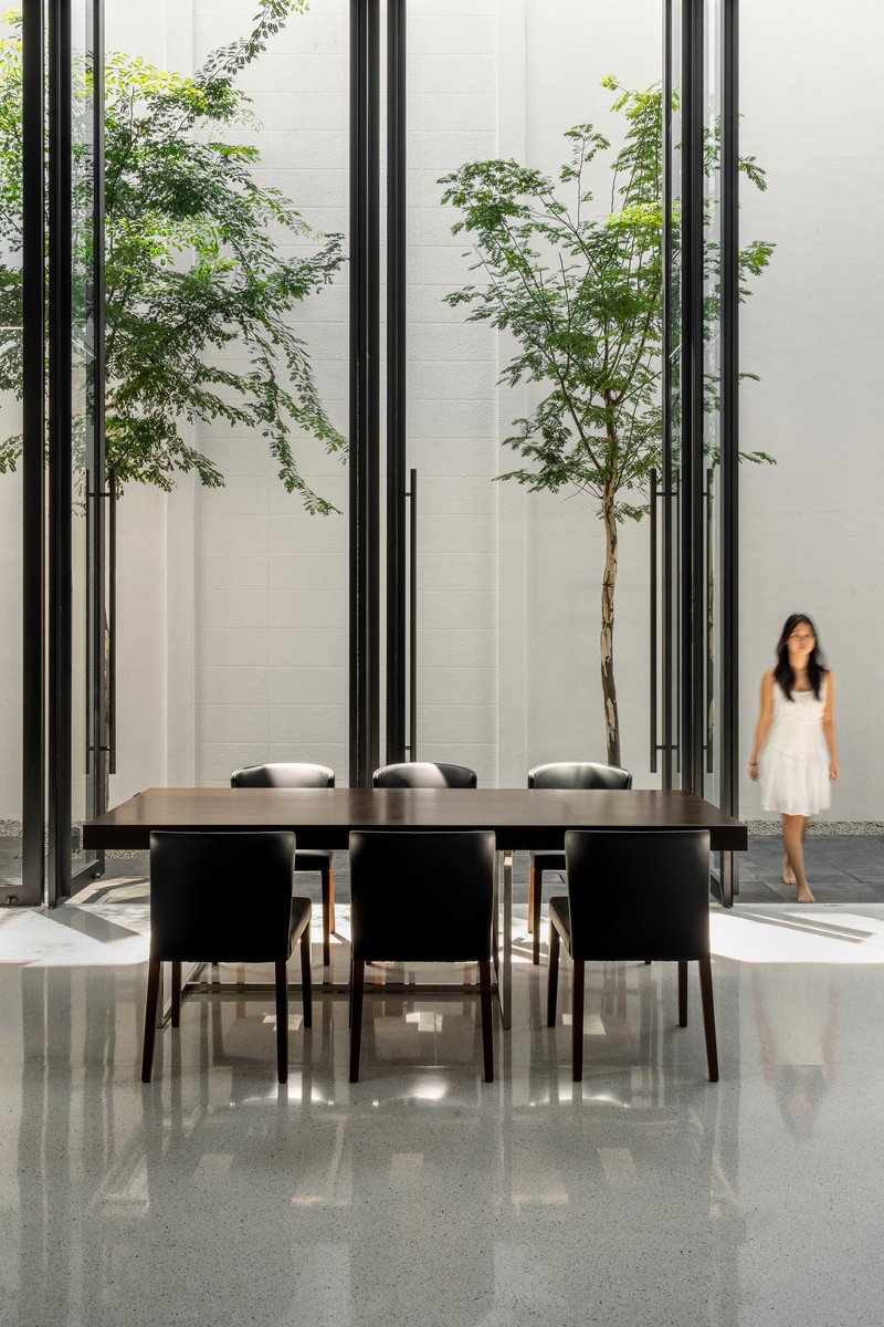 Dining table surrounded by steel frame screens with young trees and a figure in the courtyard