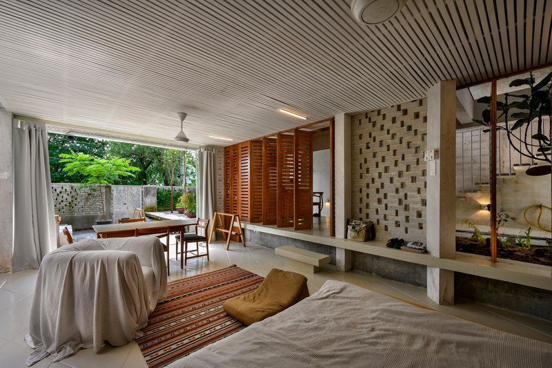 Living area with slatted ceiling opening to a planted terrace framed by white curtains