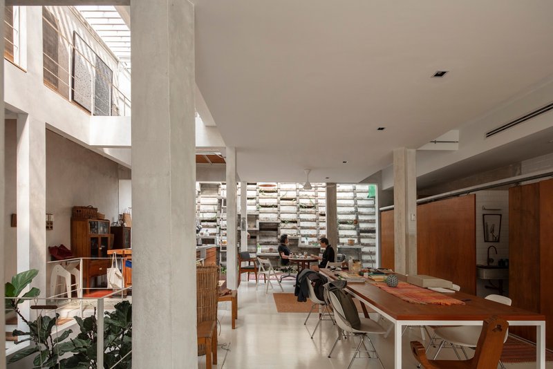 Double-height interior with concrete columns, timber dining table, and horizontal louvered screen wall with planted shelves