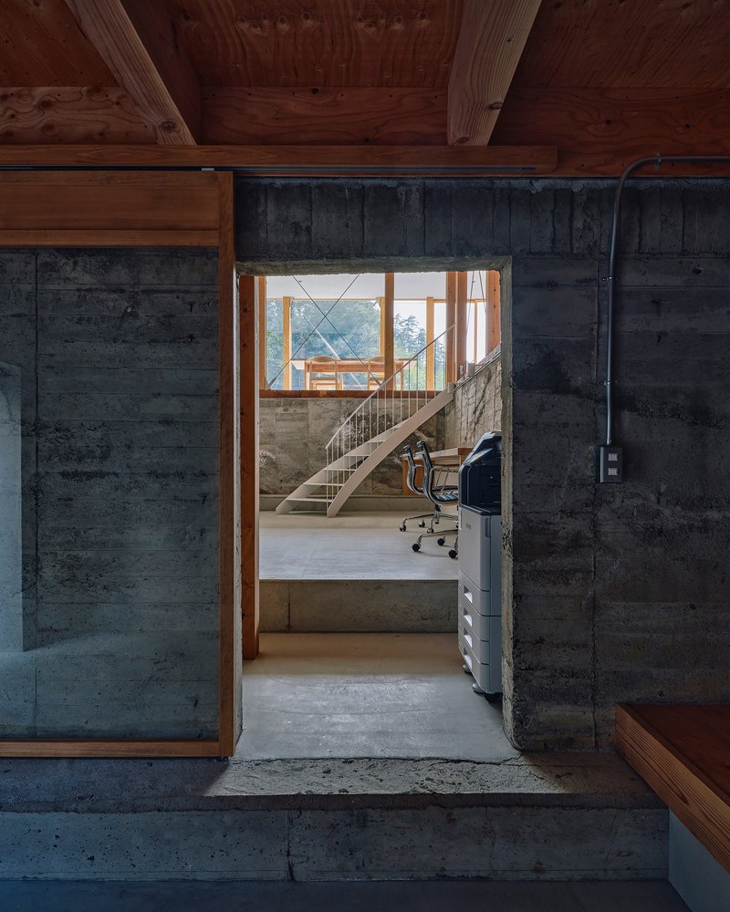 View through a timber doorway into a workspace with board-formed concrete walls and exposed timber ceiling