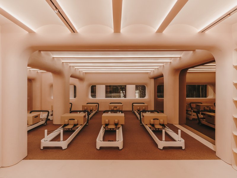 Exercise studio with rows of reformer machines beneath curved arches and cove-lit ceiling beams in warm tones