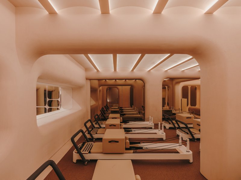 View through rounded archway showing aligned reformer equipment and recessed lighting in the ribbed ceiling