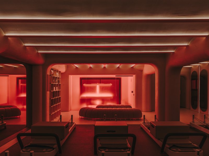 Red-lit wellness space with reformer stations facing arched openings and linear ceiling coves