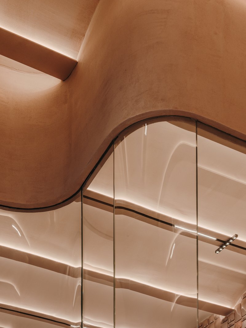 Close-up of curved plaster wall meeting sculptural ribbed glass panels with linear ceiling detail above
