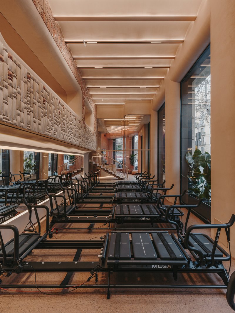 Long view down the exercise studio showing timber ceiling beams and woven wall panels flanking equipment rows