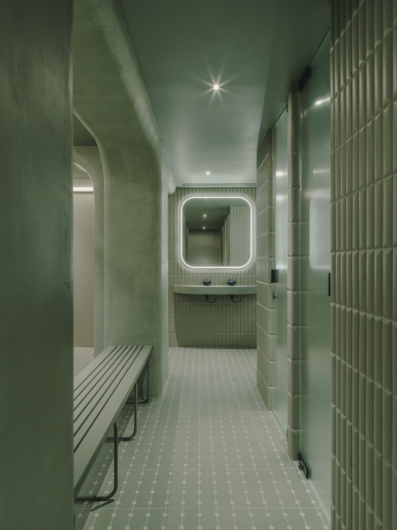 Locker room corridor with ribbed green tile walls, white mosaic floor and backlit mirror