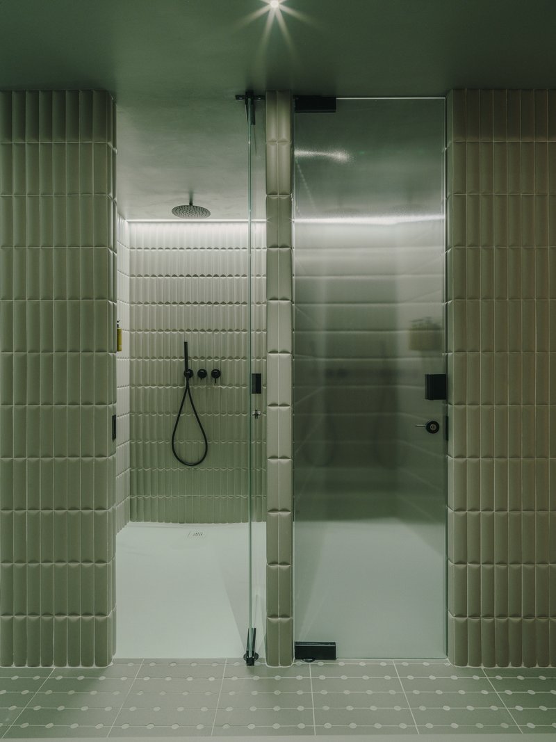 Glass-enclosed shower stall with vertical ribbed green tile and overhead rainfall showerhead