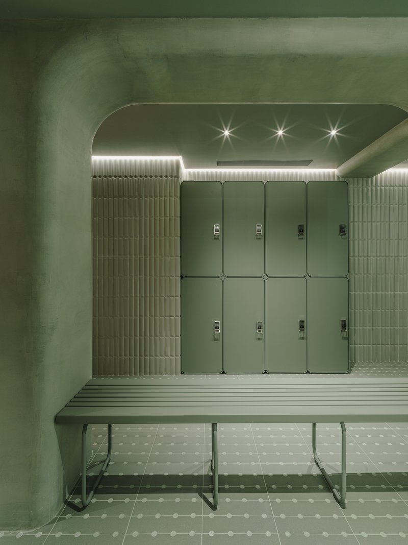 Locker alcove with slatted bench, ribbed tile walls and recessed linear lighting above