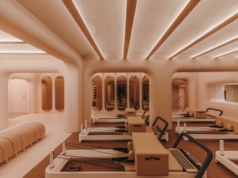 Pilates studio with rows of reformer equipment beneath arched openings and ribbed ceiling beams with uplighting