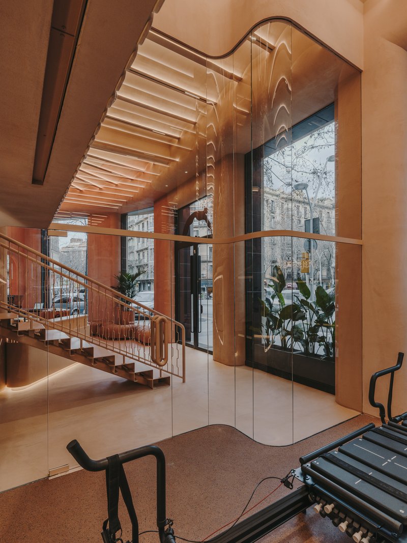Glass-enclosed stairwell with curved railings adjacent to full-height windows overlooking urban street with exercise equipment below