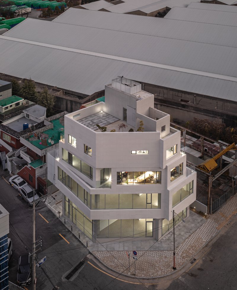 Aerial view of the corner building at dusk showing rooftop terrace and surrounding industrial sheds