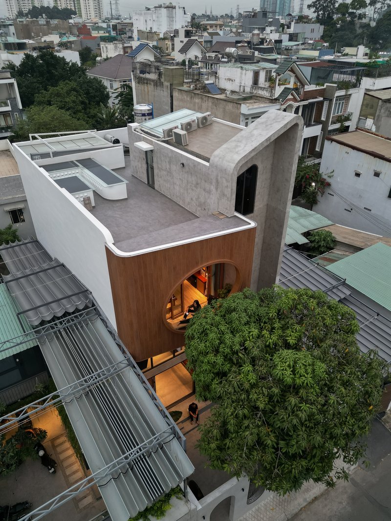 Aerial view of concrete rooftop terrace with timber-clad volume and curved opening overlooking dense neighborhood