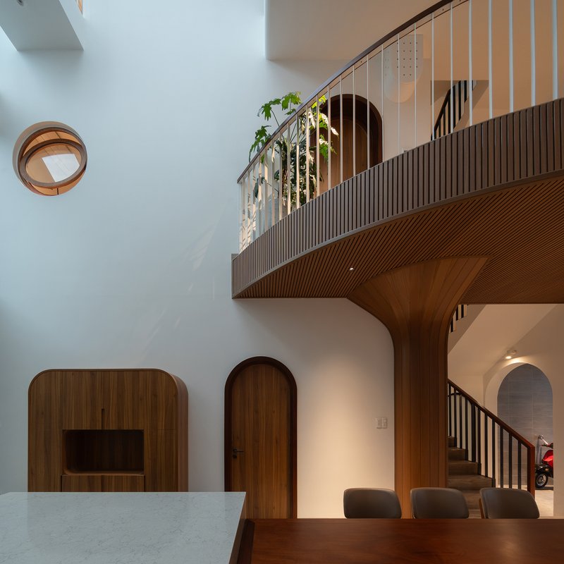 Curved timber balcony with vertical slat cladding suspended above arched doorways and dining area