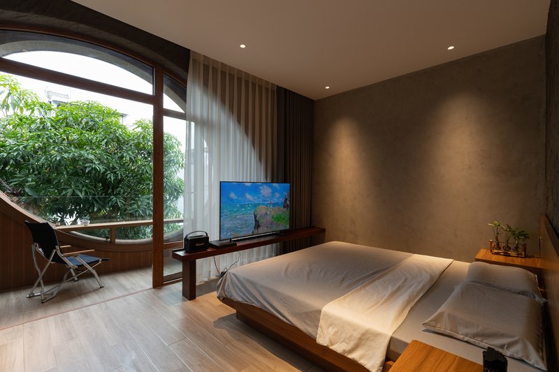Bedroom with low timber bed and arched glazing opening to a planted terrace