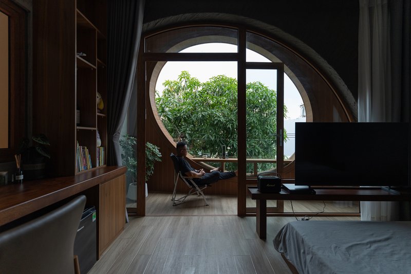 Circular window with occupant seated in a chair overlooking treetops