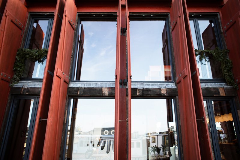 Detail of red-painted timber window frames opening outward with metal hinges and stone sills