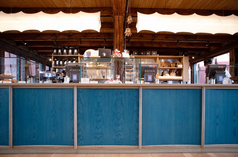 Service counter with blue-stained wood panels below glass display cases and exposed timber ceiling beams