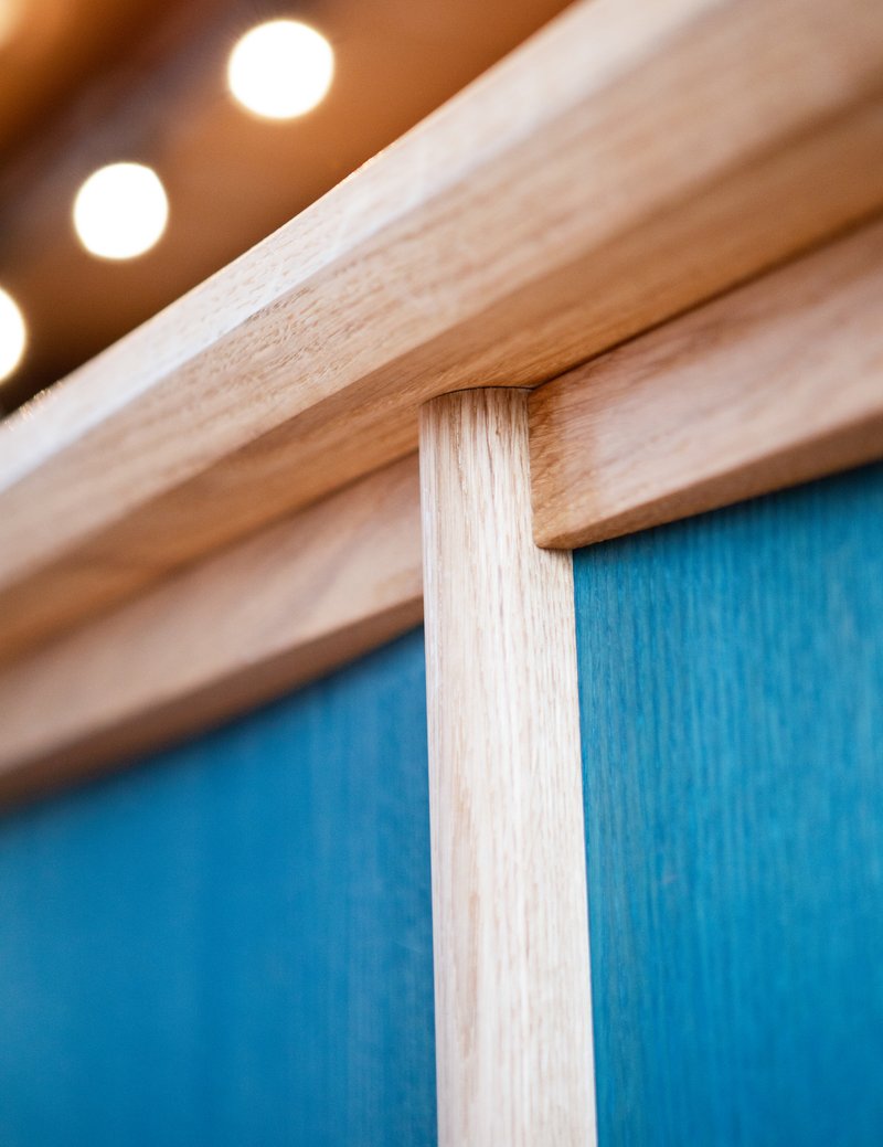 Detail of light wood frame joinery against a blue-stained wood panel with warm lighting above