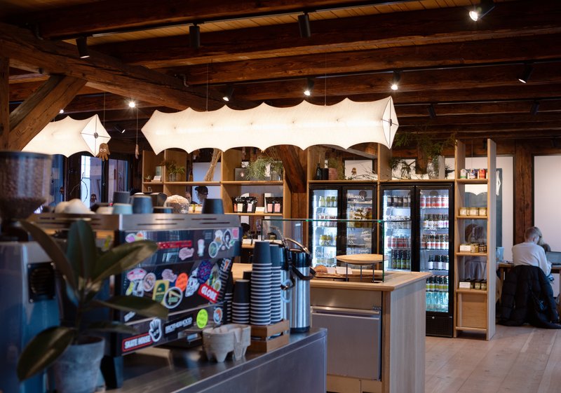 Interior view of cafe counter with refrigerated cases, retail shelving and heavy timber trusses overhead