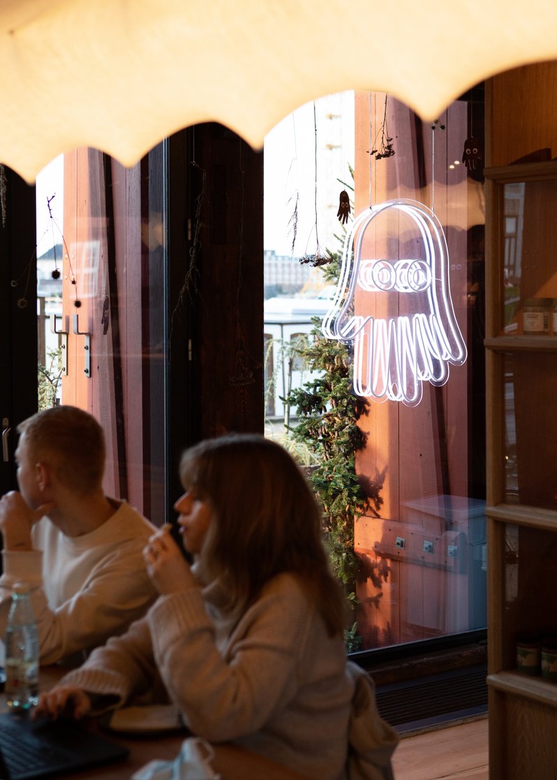 Interior view through arched openings with neon sign and diners seated near glazed facade at dusk