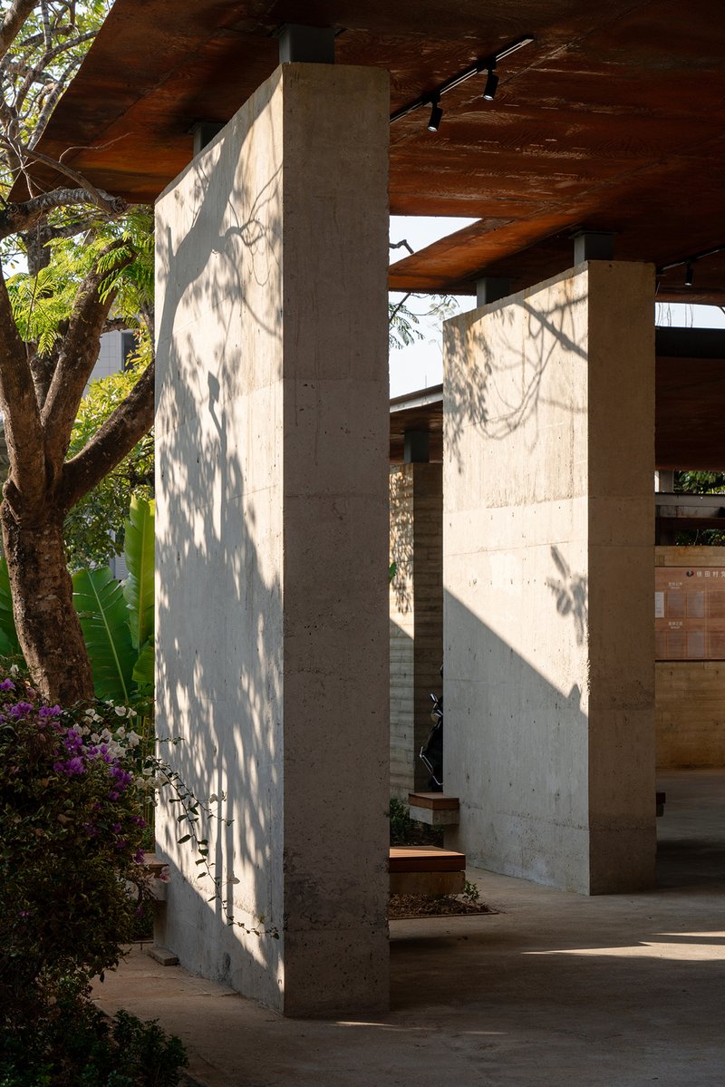 Concrete columns with dappled tree shadows beneath a timber plank soffit at an exterior covered passage