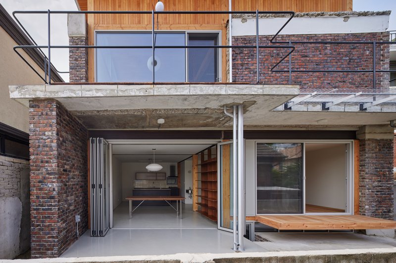 Ground level view showing folding corrugated doors opening beneath a concrete balcony with steel railings and timber cladding above