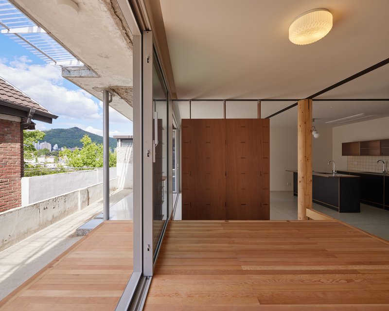 Interior view through sliding glass doors to the timber terrace with brise-soleil above and green mountains beyond