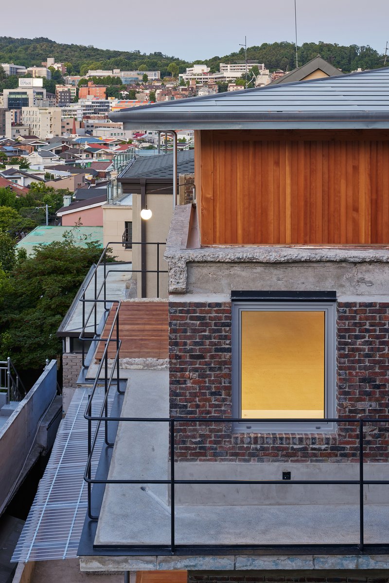 Rooftop terrace with timber pavilion and illuminated window in brick base at twilight