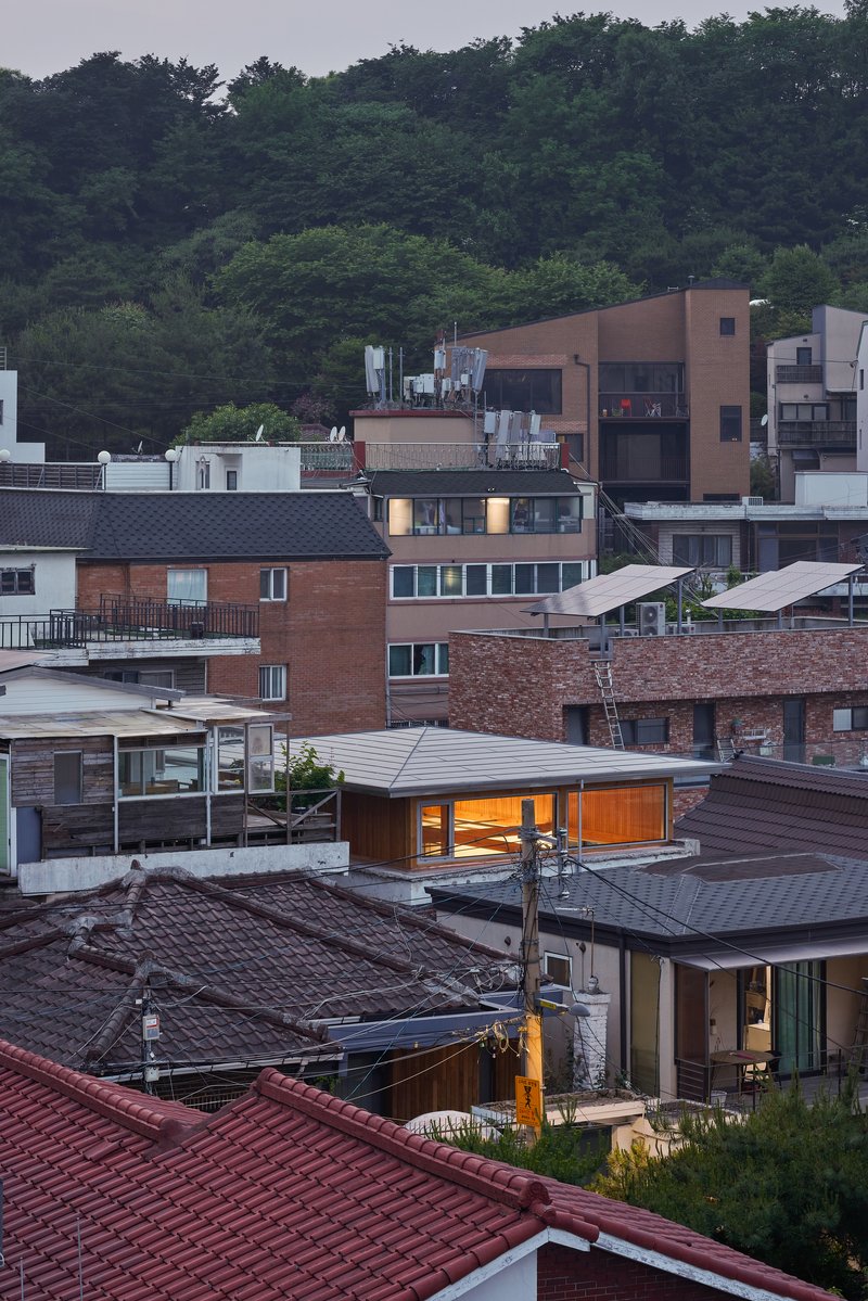 Rooftop view of the illuminated upper level nestled among tiled roofs and hillside greenery