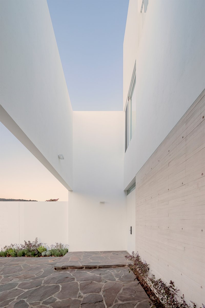 Sloped passage with board-formed concrete wall and narrow skylight overhead at twilight