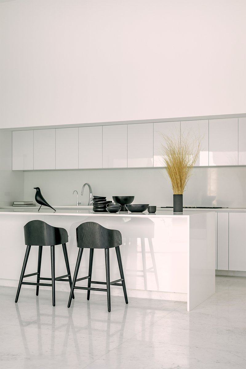 Kitchen island with black bar stools and decorative wheat stems against white cabinetry and terrazzo floor