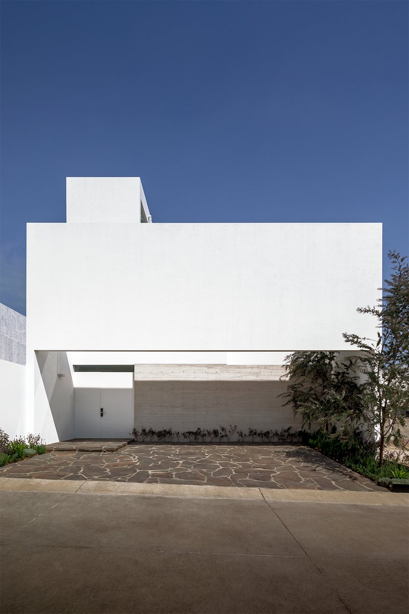 White stucco facade with cantilevered carport above irregular stone pavers under clear blue sky