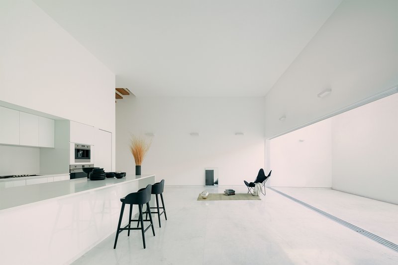 Open-plan living space with kitchen island, black stools and sliding glass wall to courtyard