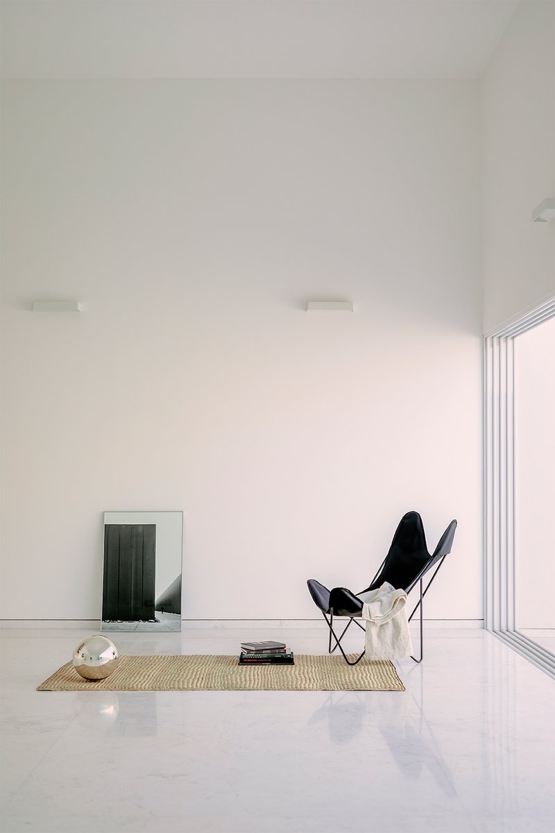 Sitting area with butterfly chair on woven rug beside floor-to-ceiling folding glass doors