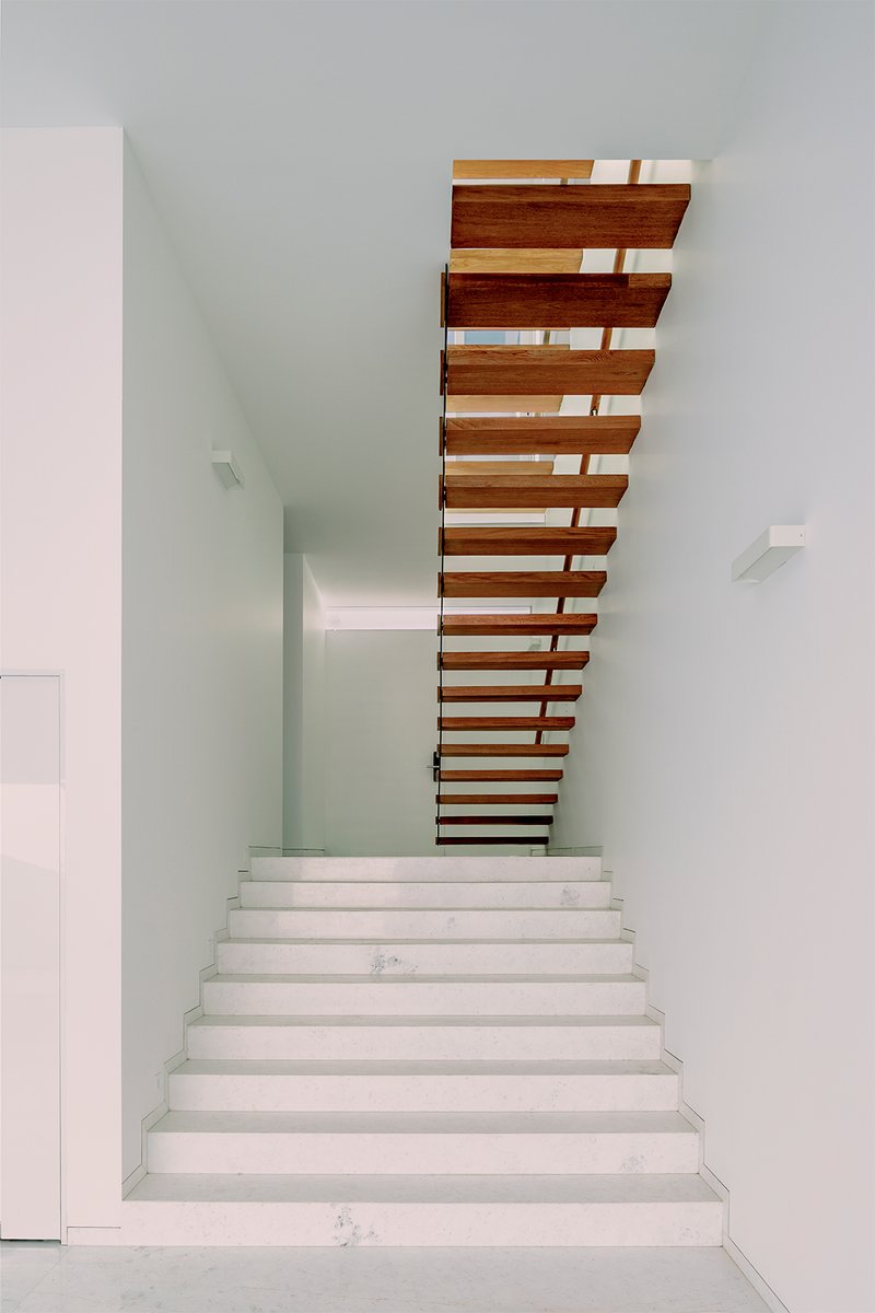 White terrazzo staircase with floating timber treads ascending through a double-height void