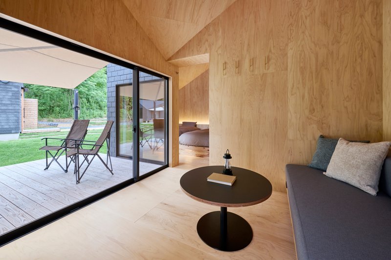 Plywood interior with vaulted ceiling and corner glazing opening to lawn and adjacent volumes