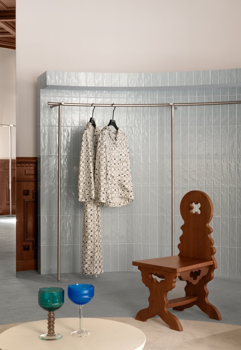 Pale blue ceramic tile wall with metal clothing rail and patterned garments hanging above concrete floor