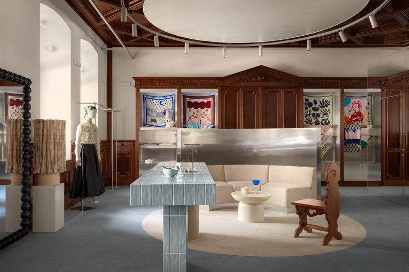 Gallery space with wood paneling, circular ceiling detail and ribbed metal furniture under track lighting