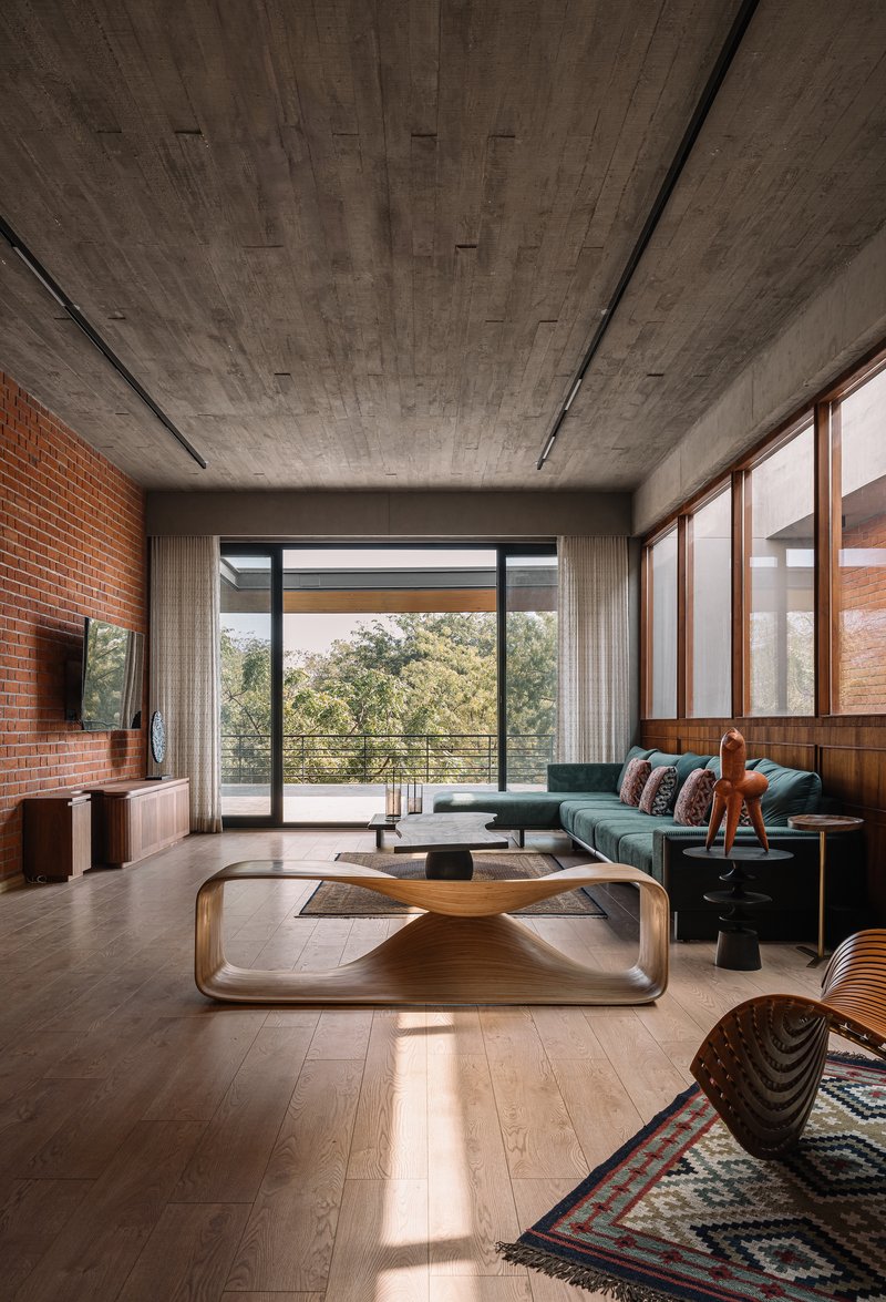 Living room with board-formed concrete ceiling, exposed brick wall, and glazed doors opening to treetops