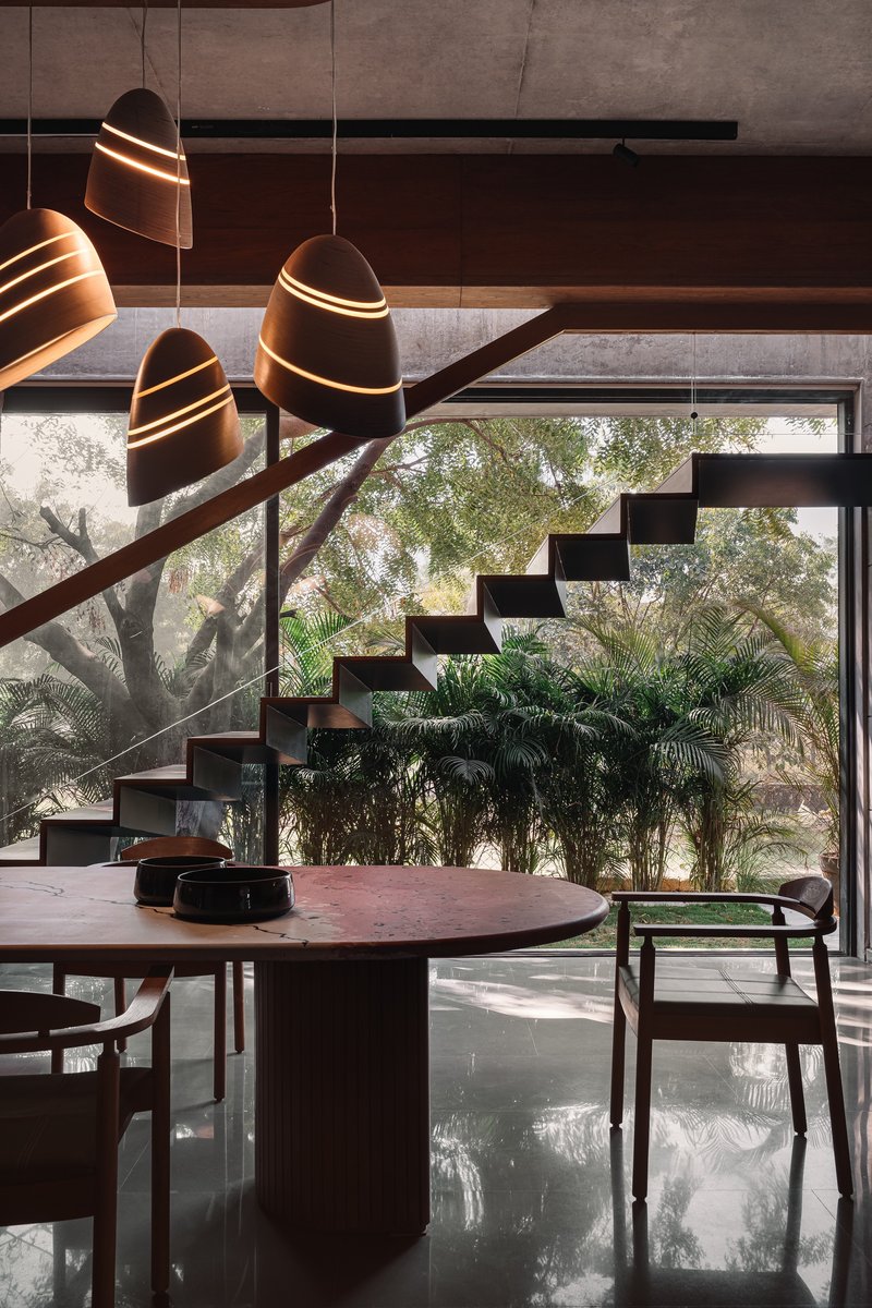 Dining area beneath cantilevered timber staircase with sculptural pendant lights and view to courtyard plantings