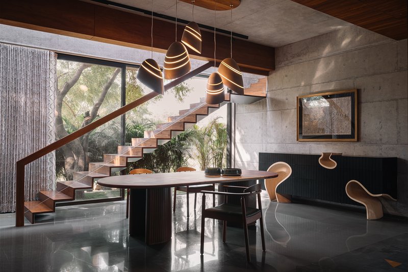 Open space showing sculptural staircase, concrete walls, polished stone floor with triangular inlays, and clustered pendant lights