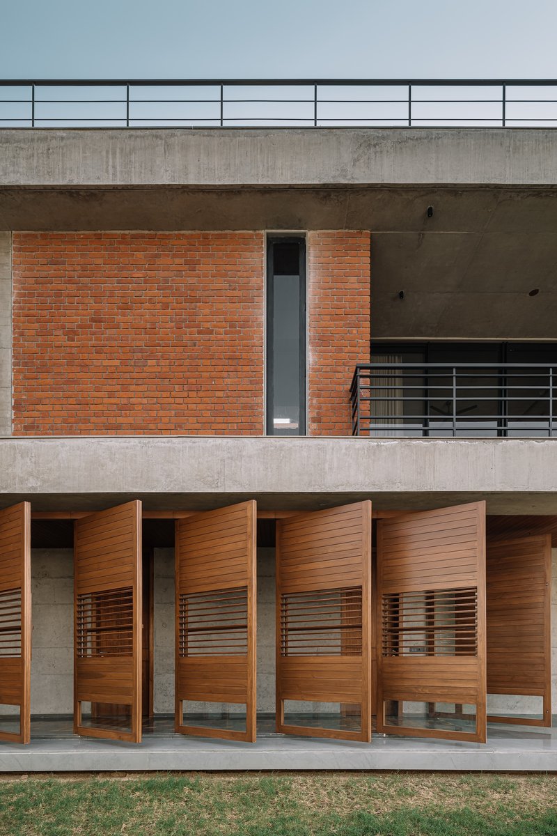 Stacked terraces with red brick wall, concrete soffits, and four timber pivot doors beneath horizontal railings