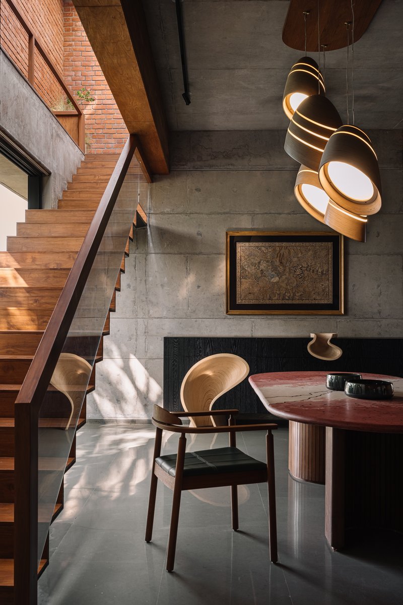 Double-height dining space with timber staircase, clustered pendant lights, and sunlight across polished concrete floor