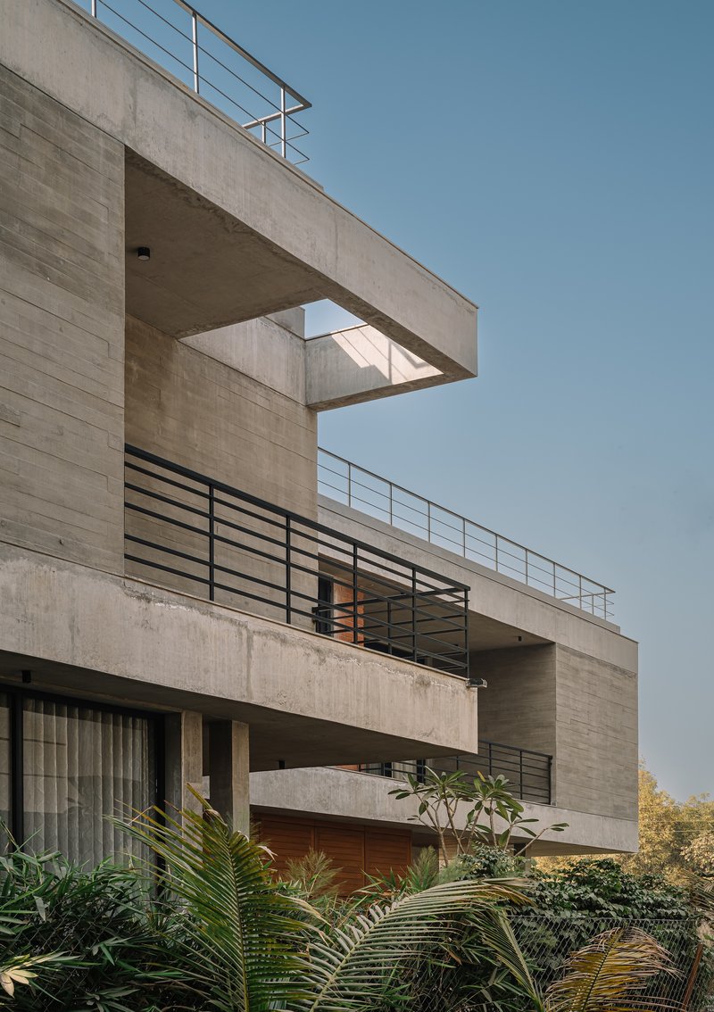 Stacked concrete balconies with horizontal steel railings and timber screens among tropical foliage below