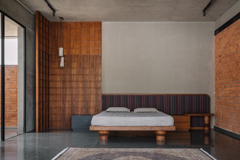 Platform bed with cylindrical timber legs centered between gridded wood paneling and exposed brick walls