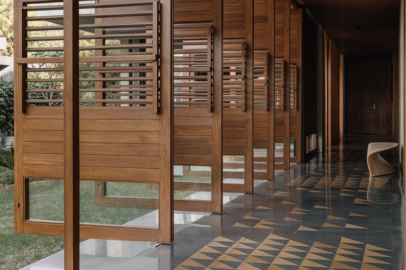 Covered corridor with pivoting timber louvered screens opening onto a lawn and patterned terrazzo floor