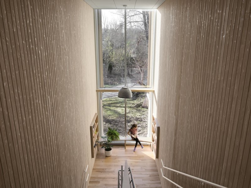 View down a timber staircase toward a tall window framing bare winter trees and a figure below