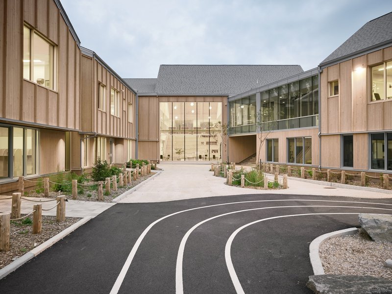 Central entrance with glazed facade and timber wings framing a curved asphalt path at twilight