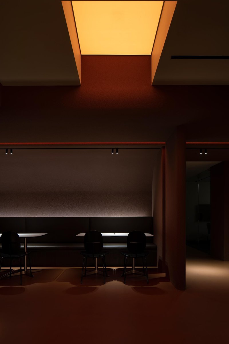 Dining area with long table beneath a recessed illuminated ceiling panel casting amber glow